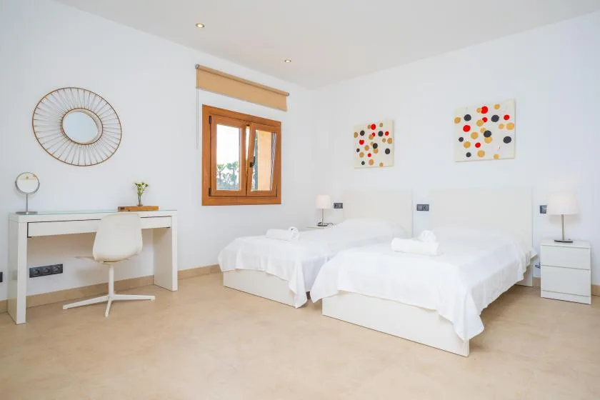 A bright bedroom with two beds, a desk, and colorful wall art.