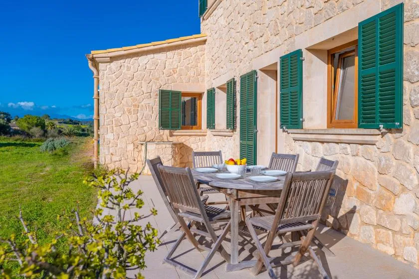 An outdoor dining area beside a stone house with green shutters.