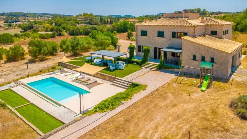 A countryside house beside a rectangular swimming pool and landscaped yard.
