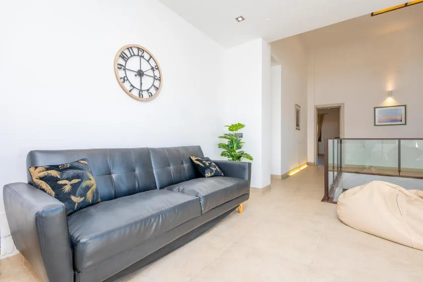 A bright living area with a gray sofa, wall clock, and potted plant.