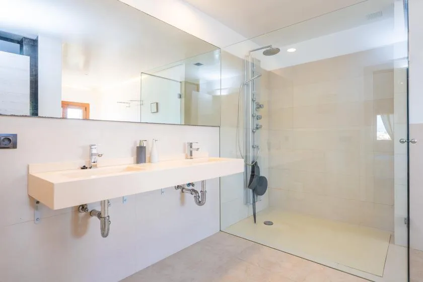 A bright bathroom with a long sink counter and glass-enclosed shower.