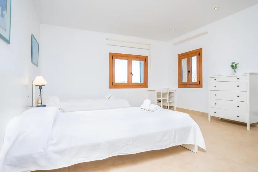 A bright bedroom with a neatly made bed and white furnishings.
