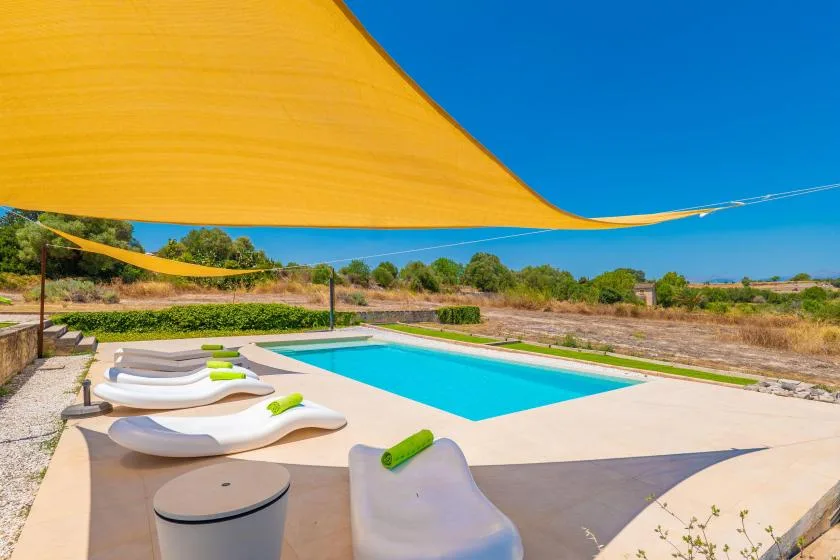 An outdoor pool and sun loungers sit beneath a large shade sail.
