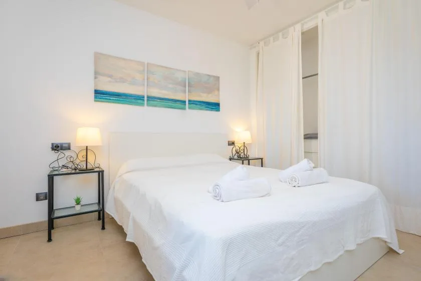 A bright bedroom with a white bed and beach artwork on the wall.