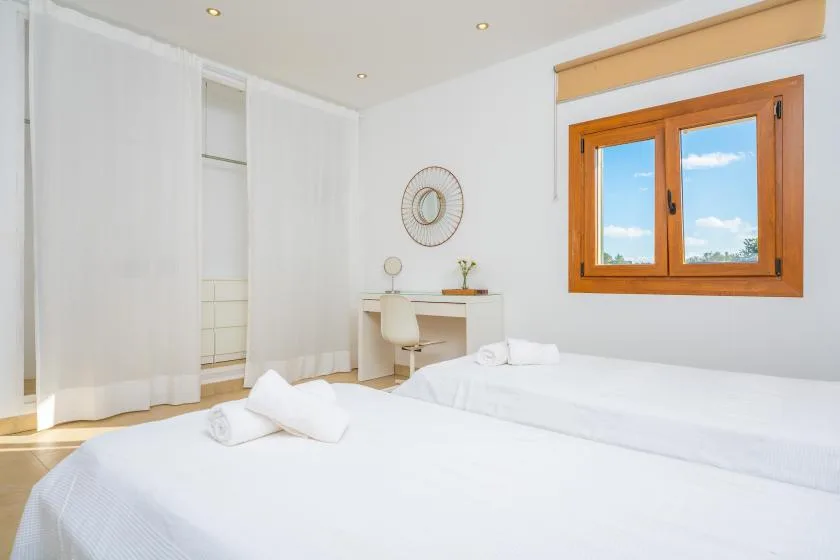 A bright bedroom with white bedding and a wooden-framed window.