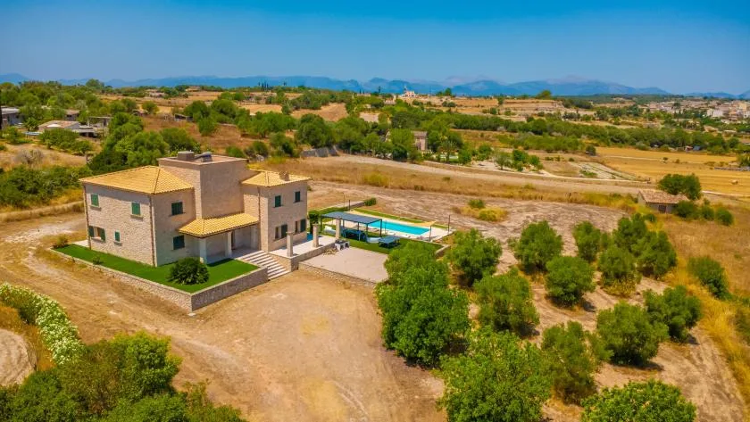 A house and swimming pool sit among trees and dry fields, with mountains in the distance.