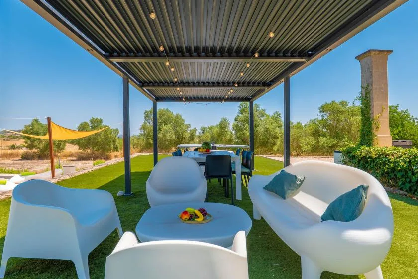 Outdoor seating beneath a covered pergola, with a table set on the lawn.