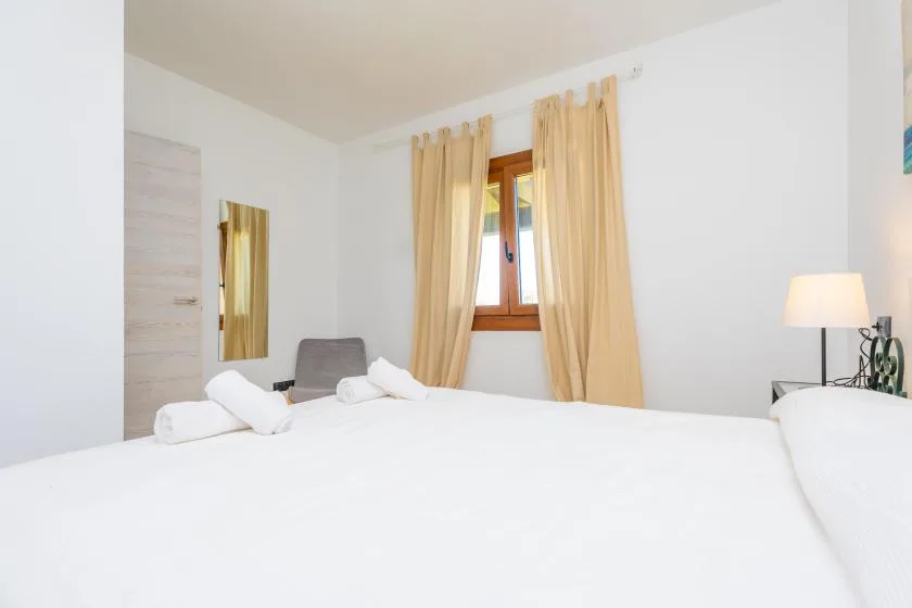 A bright bedroom with a large bed, beige curtains, and a window.