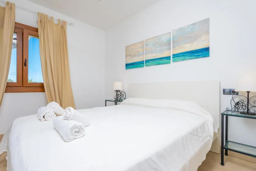 A bright bedroom with a white bed, beige curtains, and ocean-themed wall art.