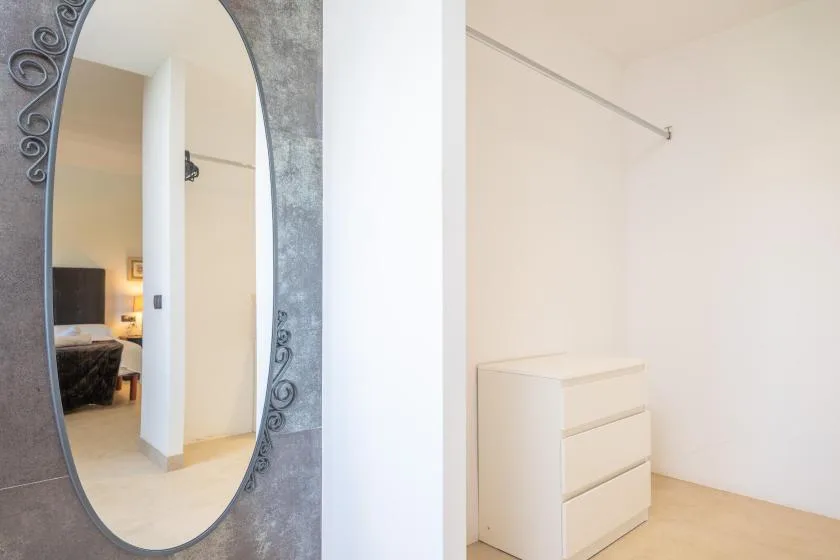 A bright dressing area with a chest of drawers and a tall oval mirror.