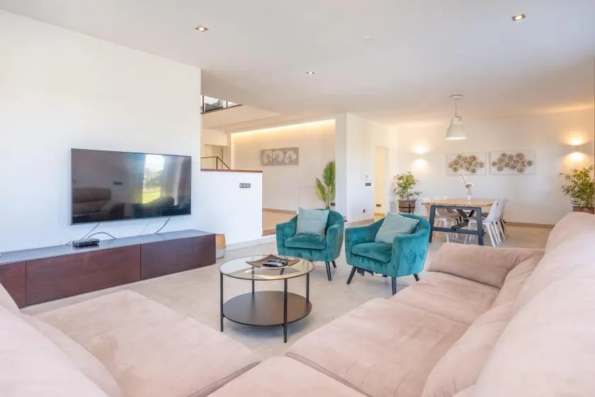 A bright living room with teal seating, a television, and an adjoining dining area.