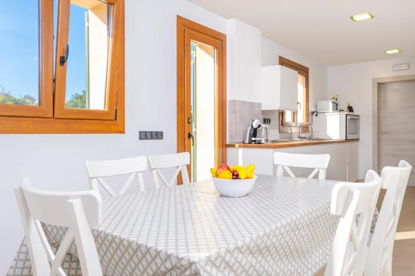 A bright dining area with a table and a compact kitchen in the background.