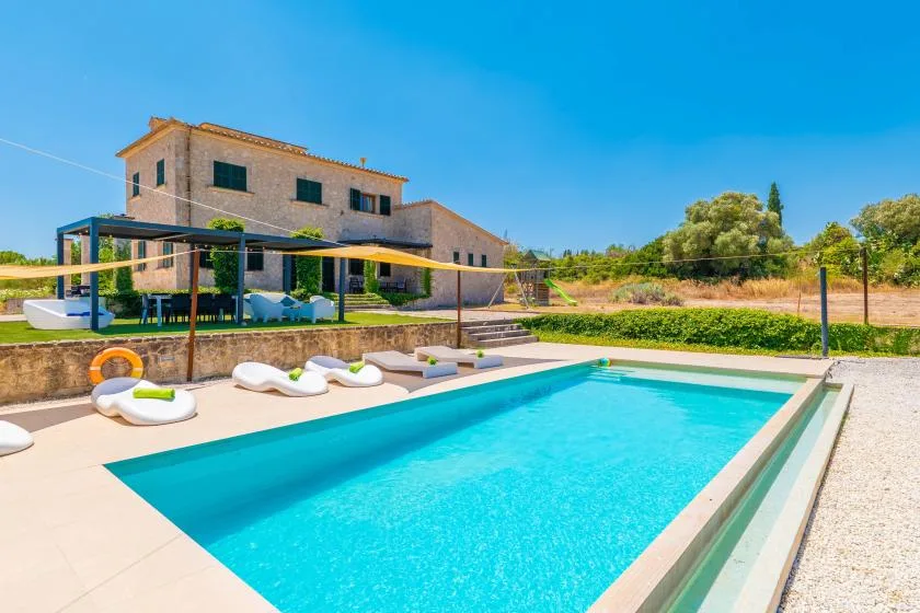 A swimming pool beside a house, with lounge seating and a shaded patio.