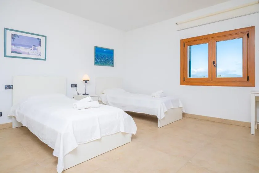 A bright bedroom with two beds and a wooden-framed window.