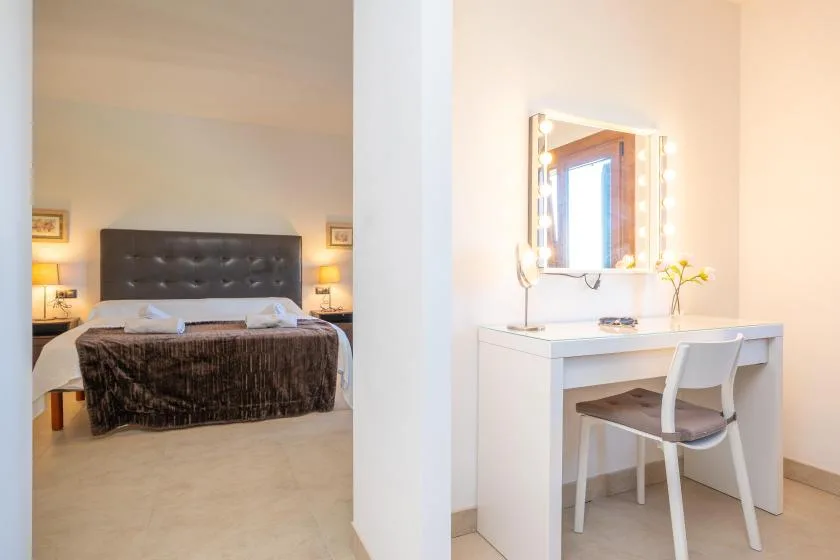 A bedroom with a bed is visible beside a white vanity and chair.