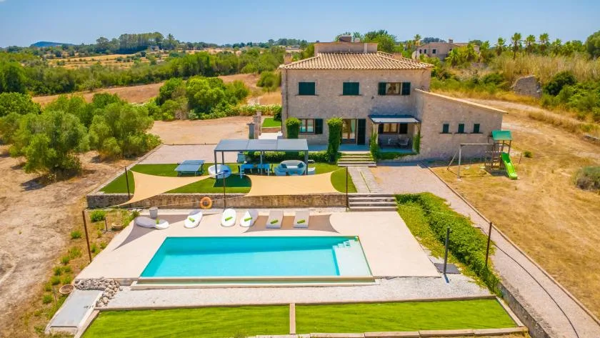 A countryside house overlooks an outdoor swimming pool and landscaped lawn.