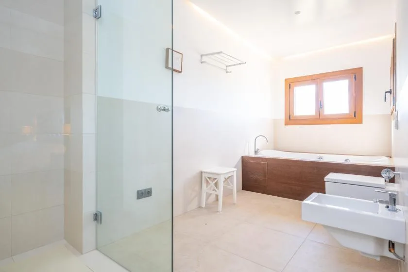 A bright bathroom with a glass shower, bathtub, and window.