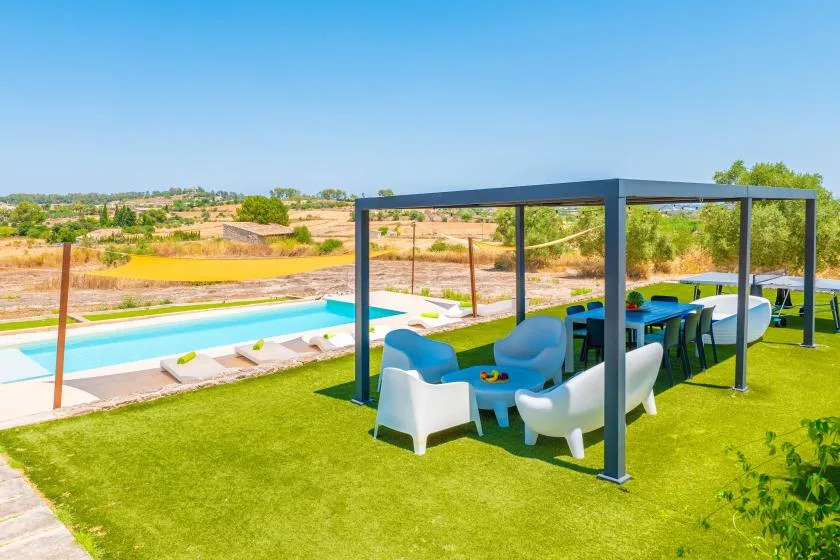 An outdoor patio with seating under a pergola overlooks a swimming pool.