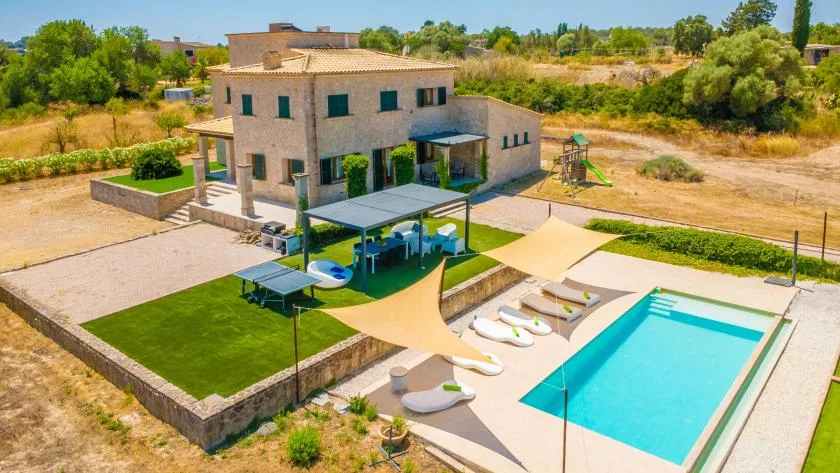 A stone house overlooks a swimming pool, shaded seating area, and small playground.