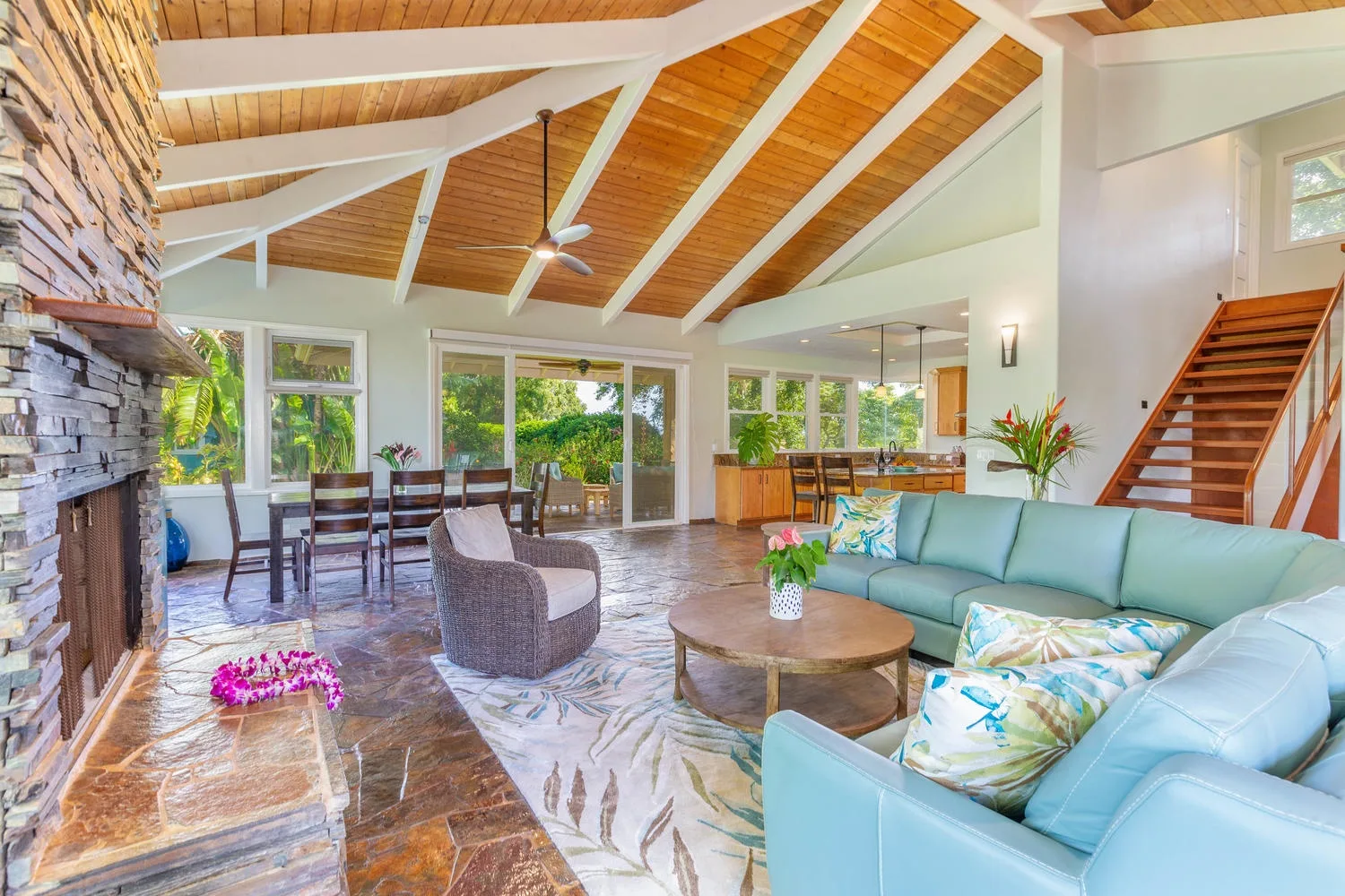 A spacious living room with seating, a dining area, and a high wooden ceiling.