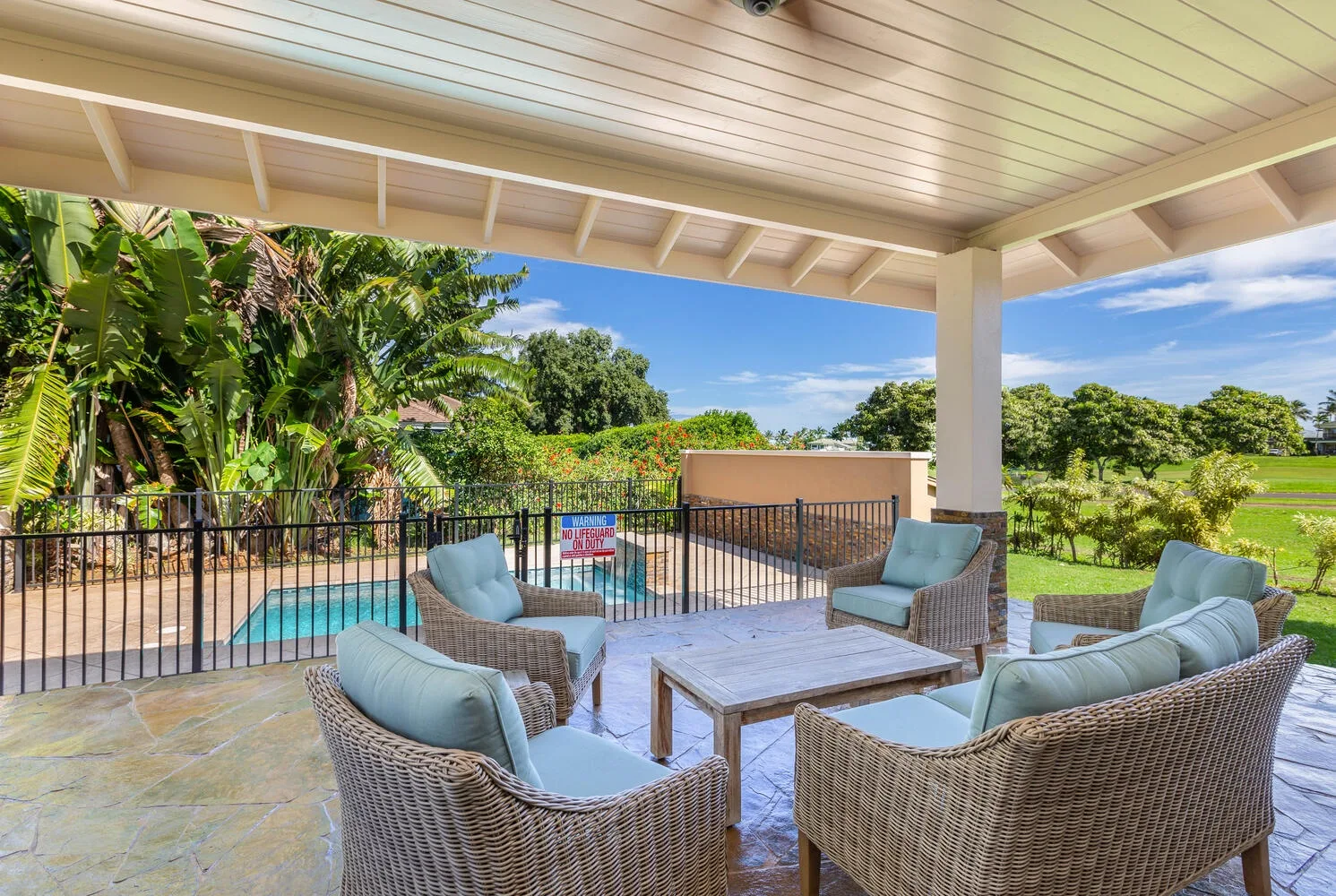 A covered outdoor patio has wicker seating beside a swimming pool.