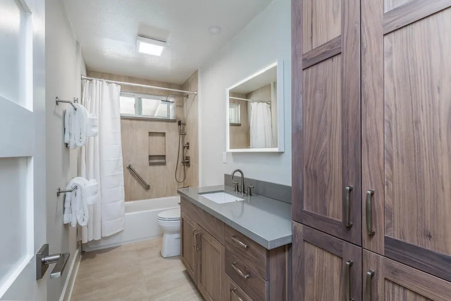 A bright bathroom with a shower, vanity, and tall wooden cabinets.
