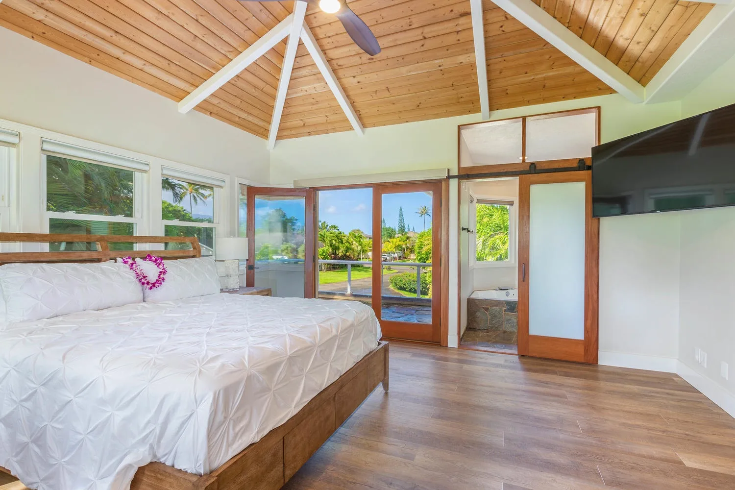 A bright bedroom with a bed, wood-paneled vaulted ceiling, and glass doors.