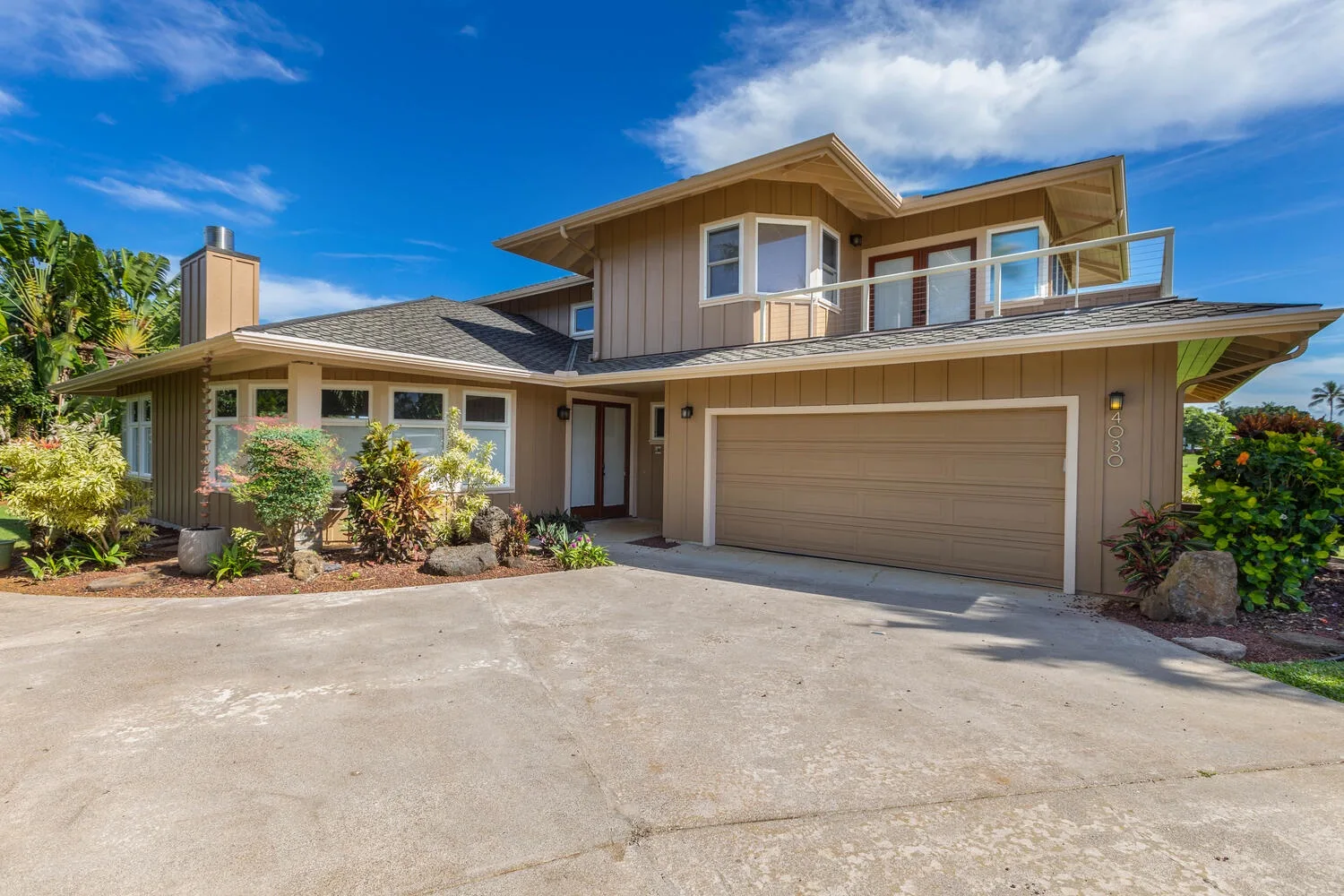 A two-story house with a wide garage and landscaped plants beside the driveway.