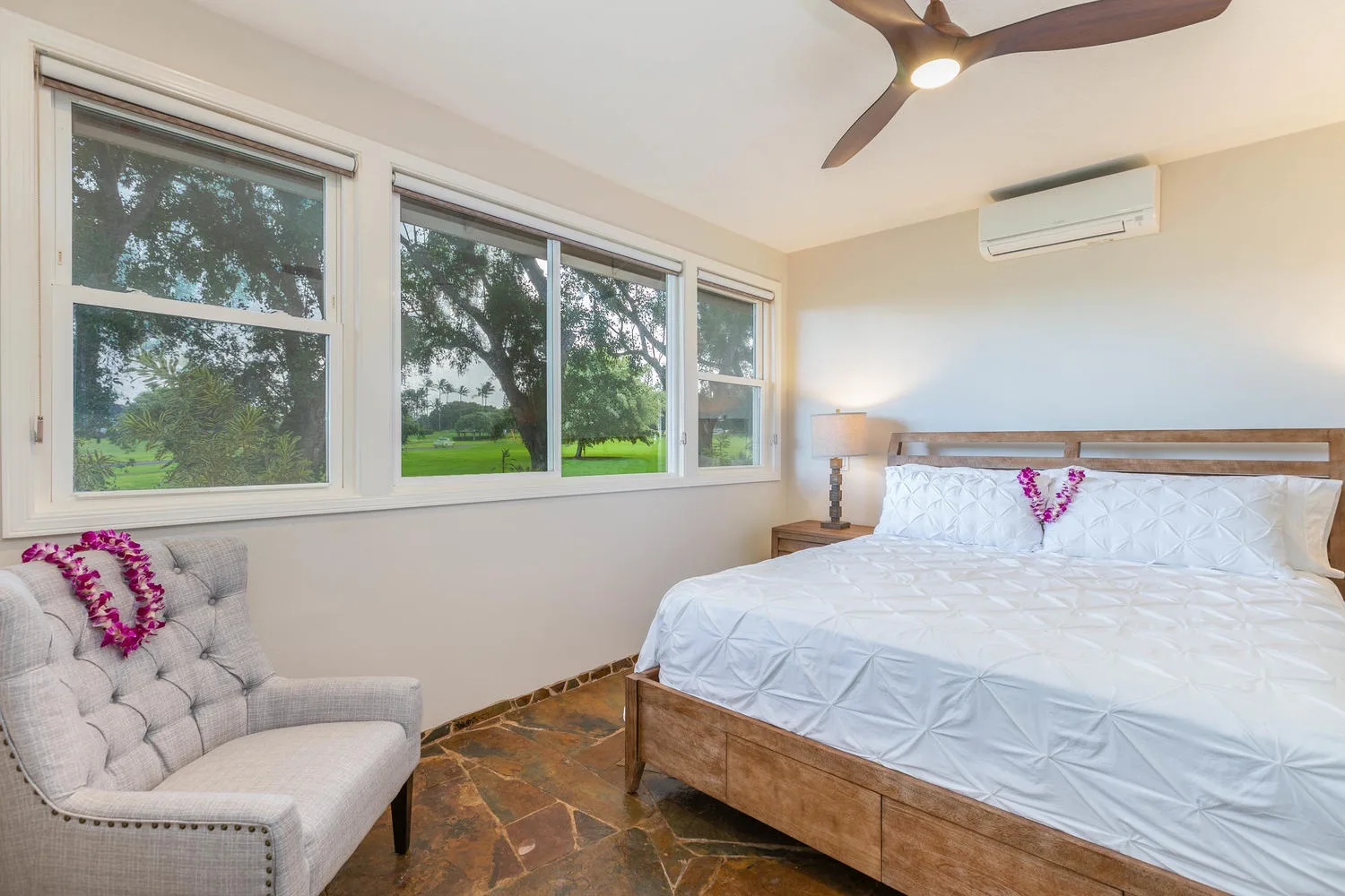 A bright bedroom with a large bed beside wide windows overlooking greenery.