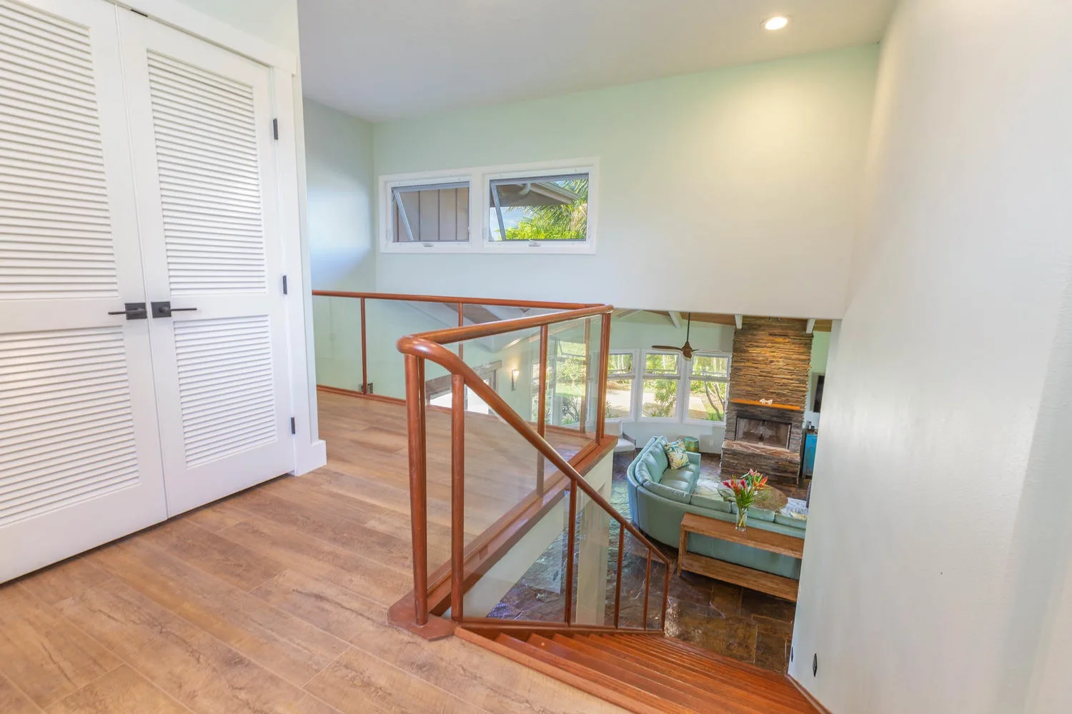An interior landing overlooks a living area, with a wooden railing beside it.