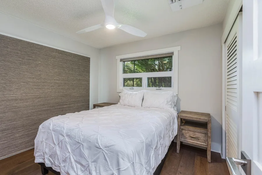 A bedroom with a bed beneath a window and a ceiling fan overhead.
