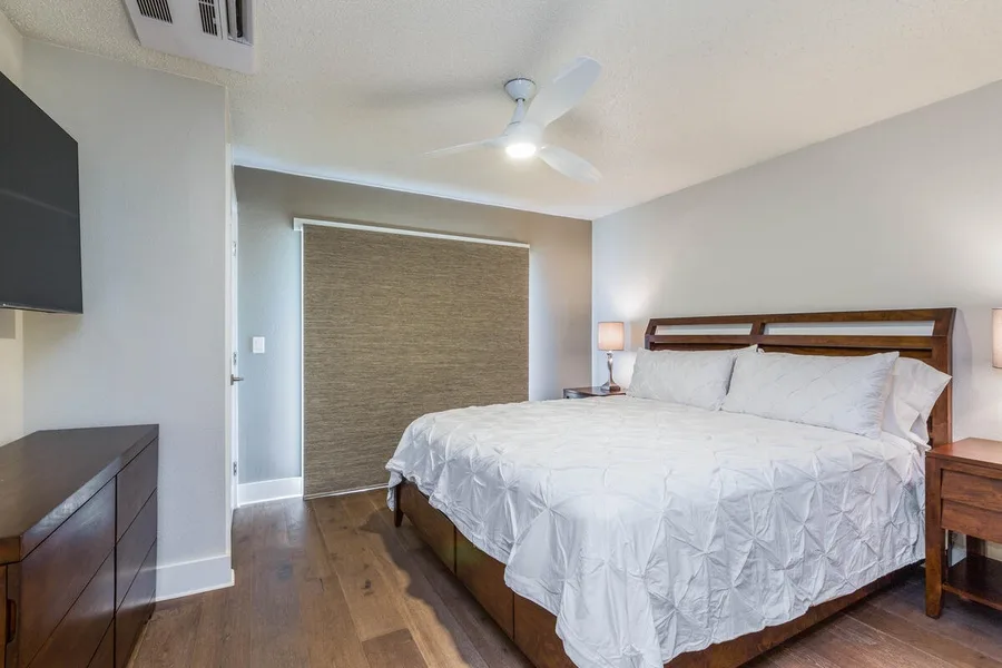 A bright bedroom with a large bed and a closed window shade.