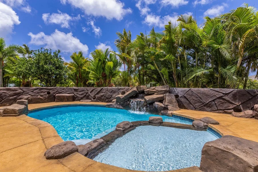 A curved outdoor pool sits beside a shallow round pool, with palms in the background.