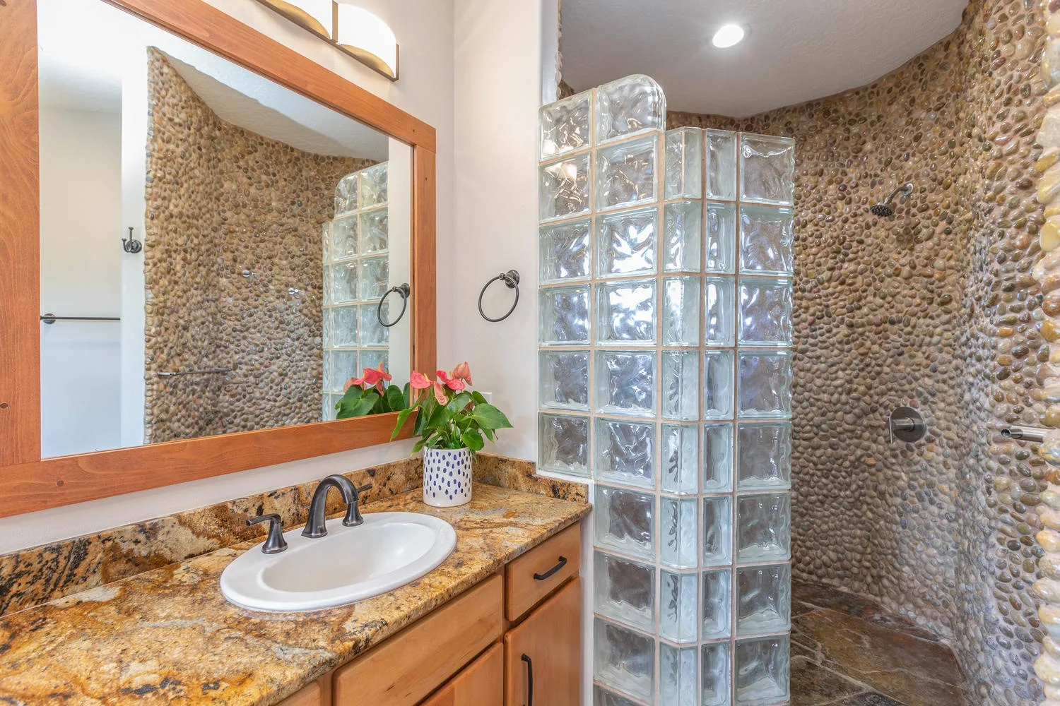 A bathroom with a sink, mirror, and glass-block shower area.