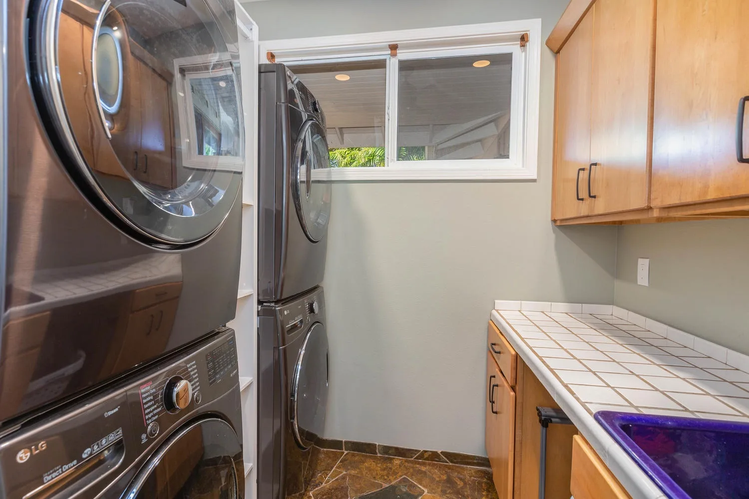 A laundry room with stacked washing machines and a tiled counter.