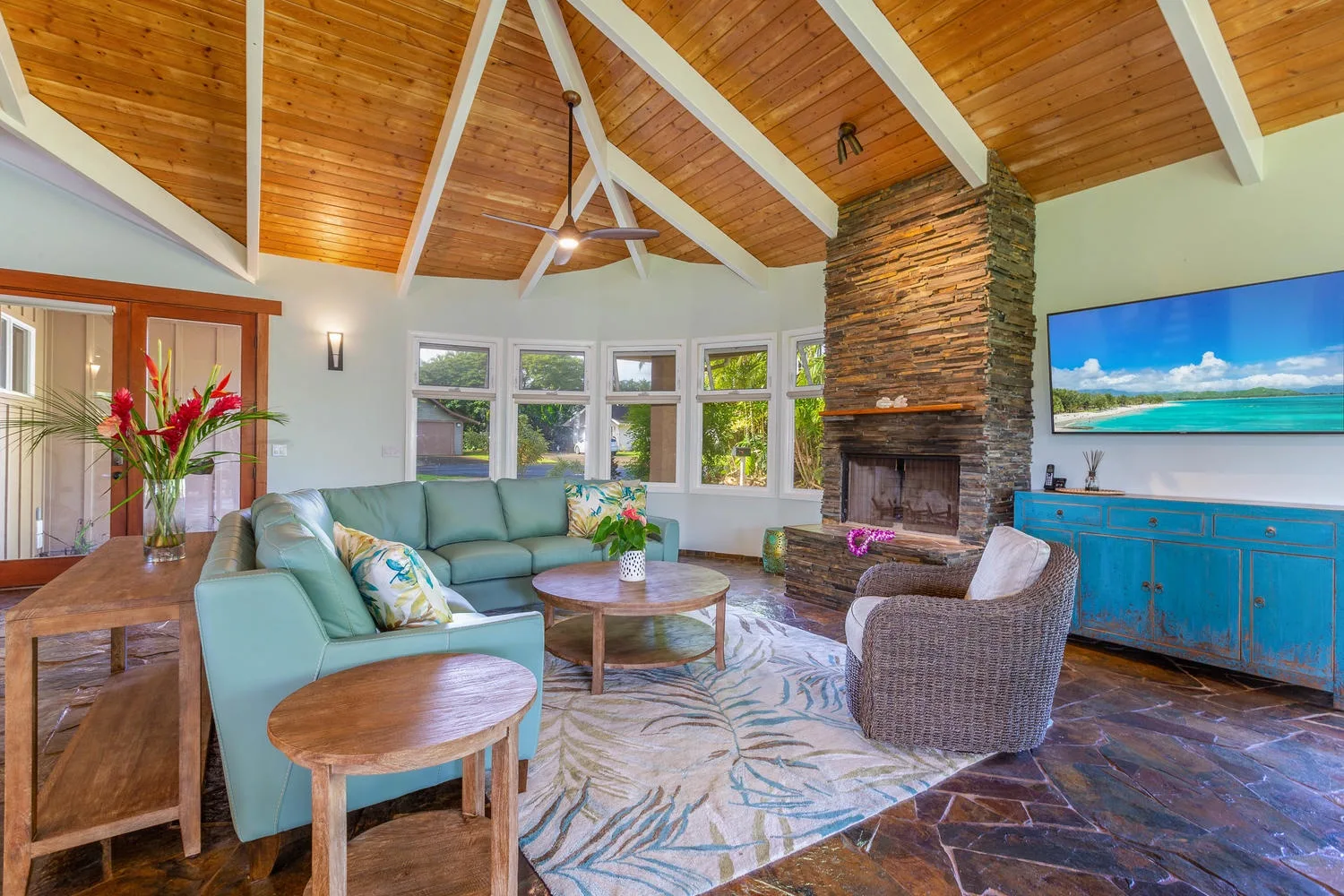 A bright living room with seating arranged around a stone fireplace.