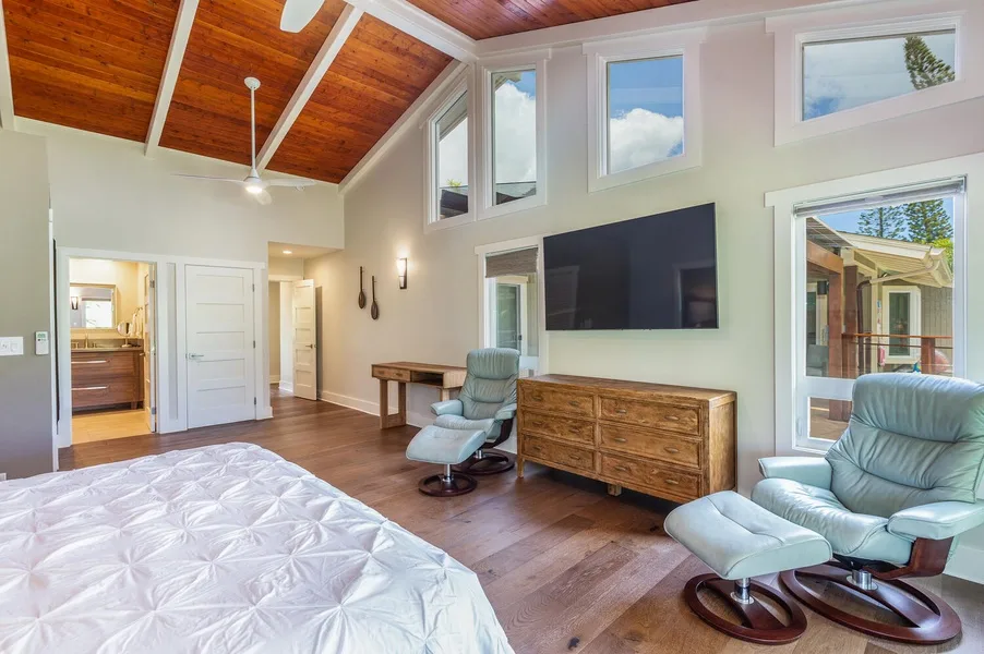 A bedroom with a bed, seating, and a television beneath a wood-paneled ceiling.