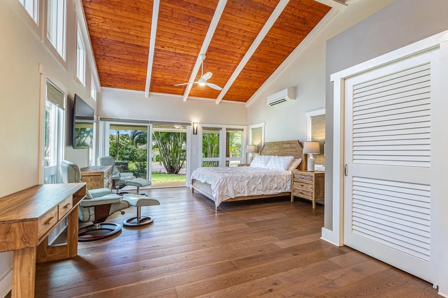 A bright bedroom with a bed, seating area, and windows opening onto greenery.