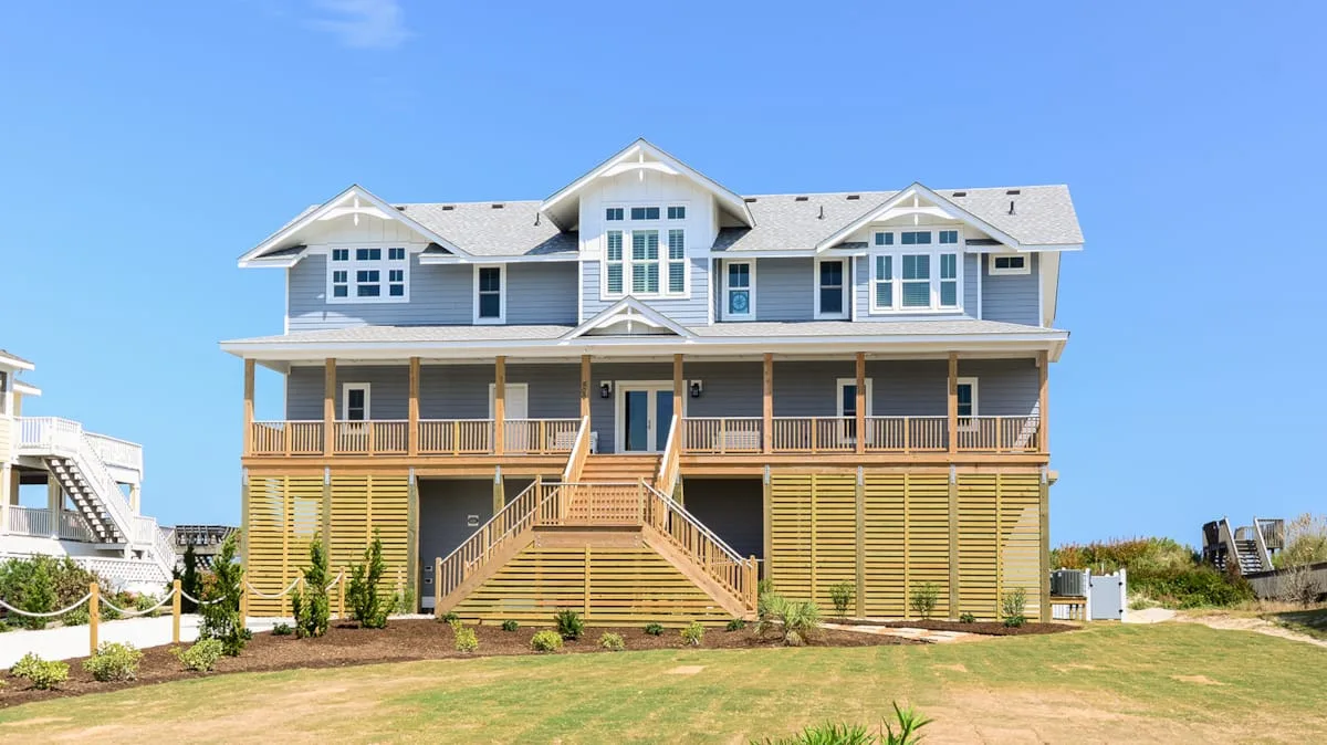 Una casa elevada de estilo costero con una amplia terraza de madera y una escalera central.