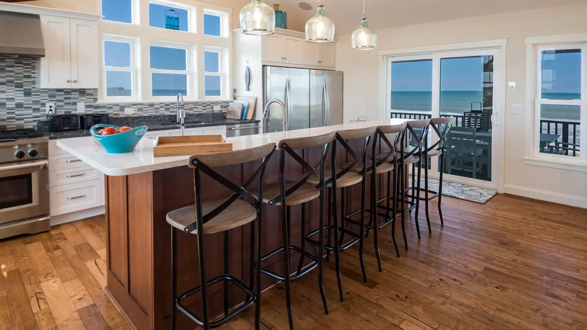 Una cocina luminosa con una isla larga y asientos junto a ventanas con vistas al agua.