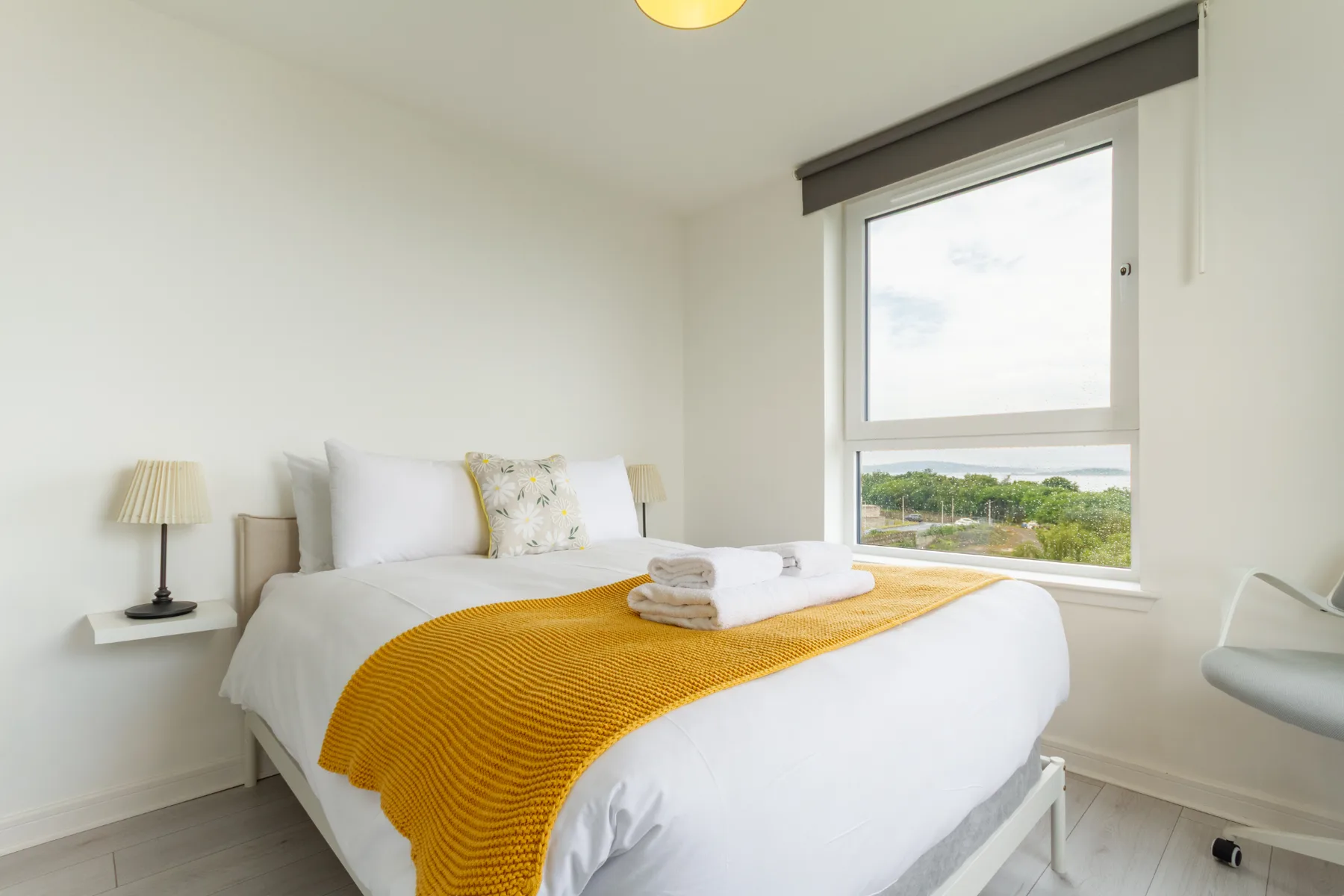 Un dormitorio luminoso con una cama bien tendida junto a una ventana grande.