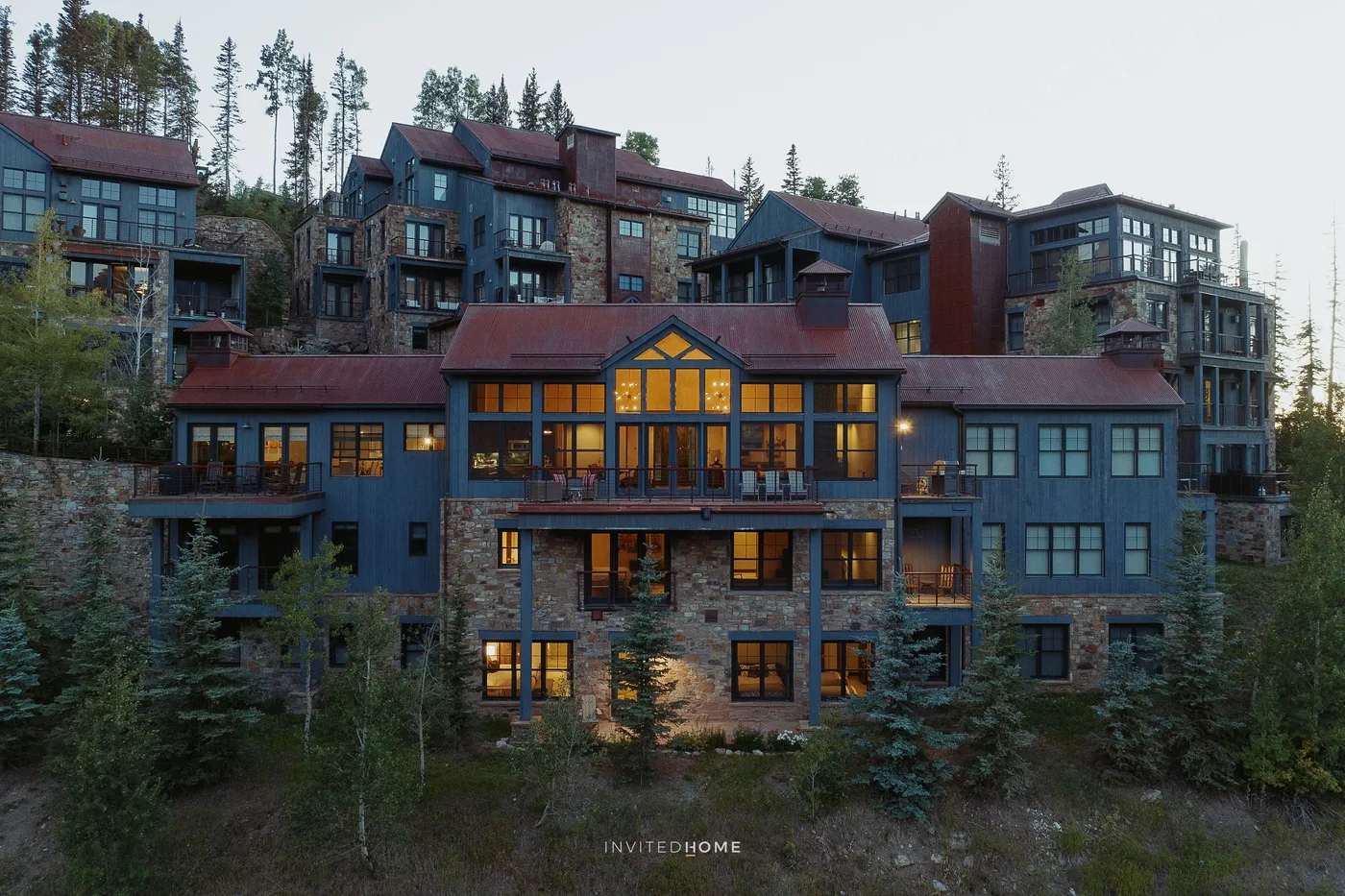 A large multi-story building with blue-gray walls and lit windows among trees.
