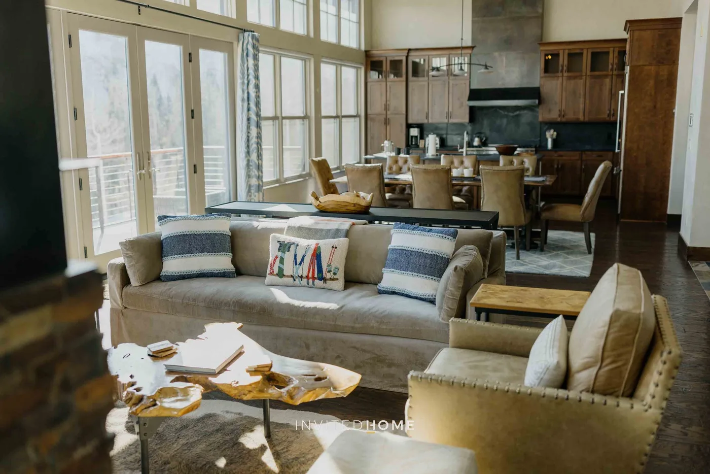 An open living and dining area with seating beside a kitchen and large windows.