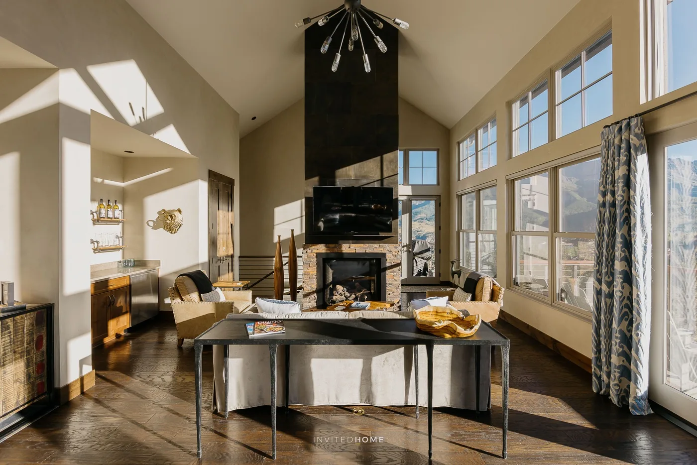 A sunlit living room with a dining table and fireplace beneath a vaulted ceiling.