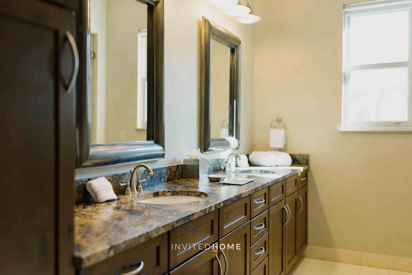 A bathroom vanity with a marble-patterned countertop, mirrors, and a window.