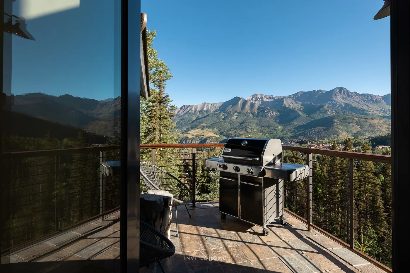 A mountain-view deck with a barbecue grill and glass doors.