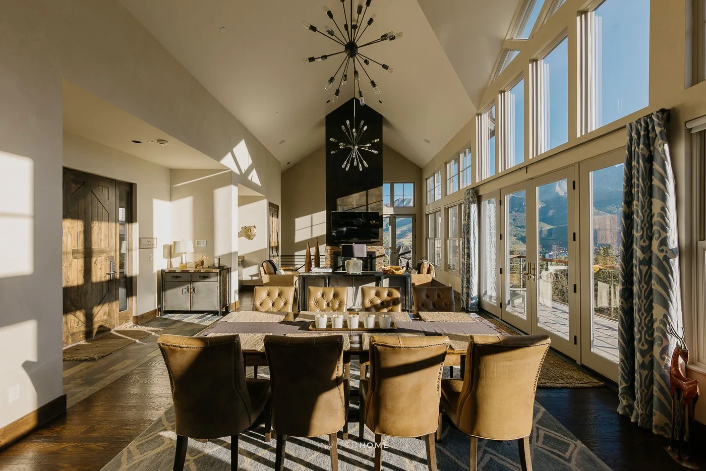 A dining area with a long table and seating beneath tall windows.