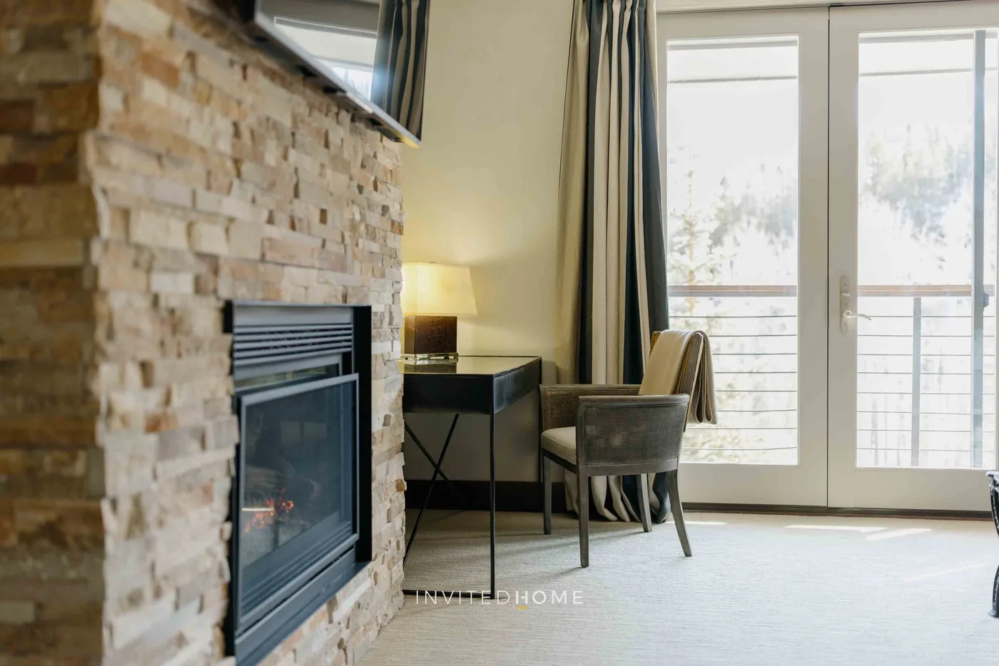 A living room with a stone fireplace, seating, and bright glass doors.