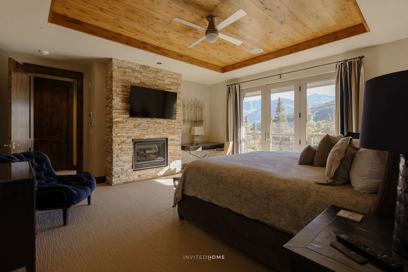 A bedroom with a large bed, stone fireplace, and mountain views through the windows.