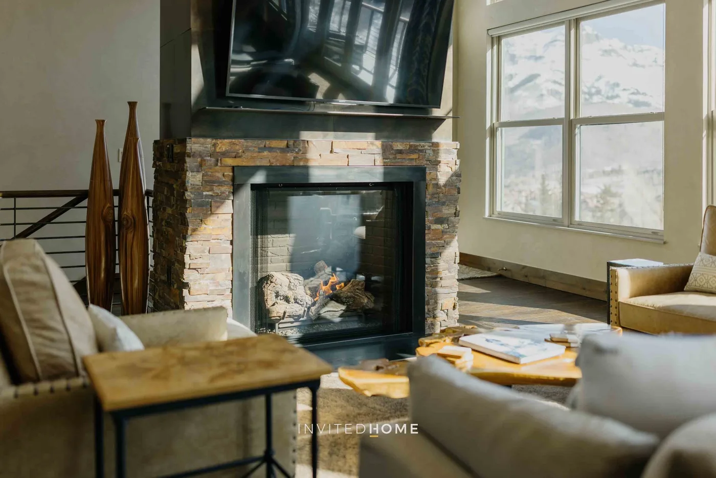 A living room with a stone fireplace, television, and large windows.